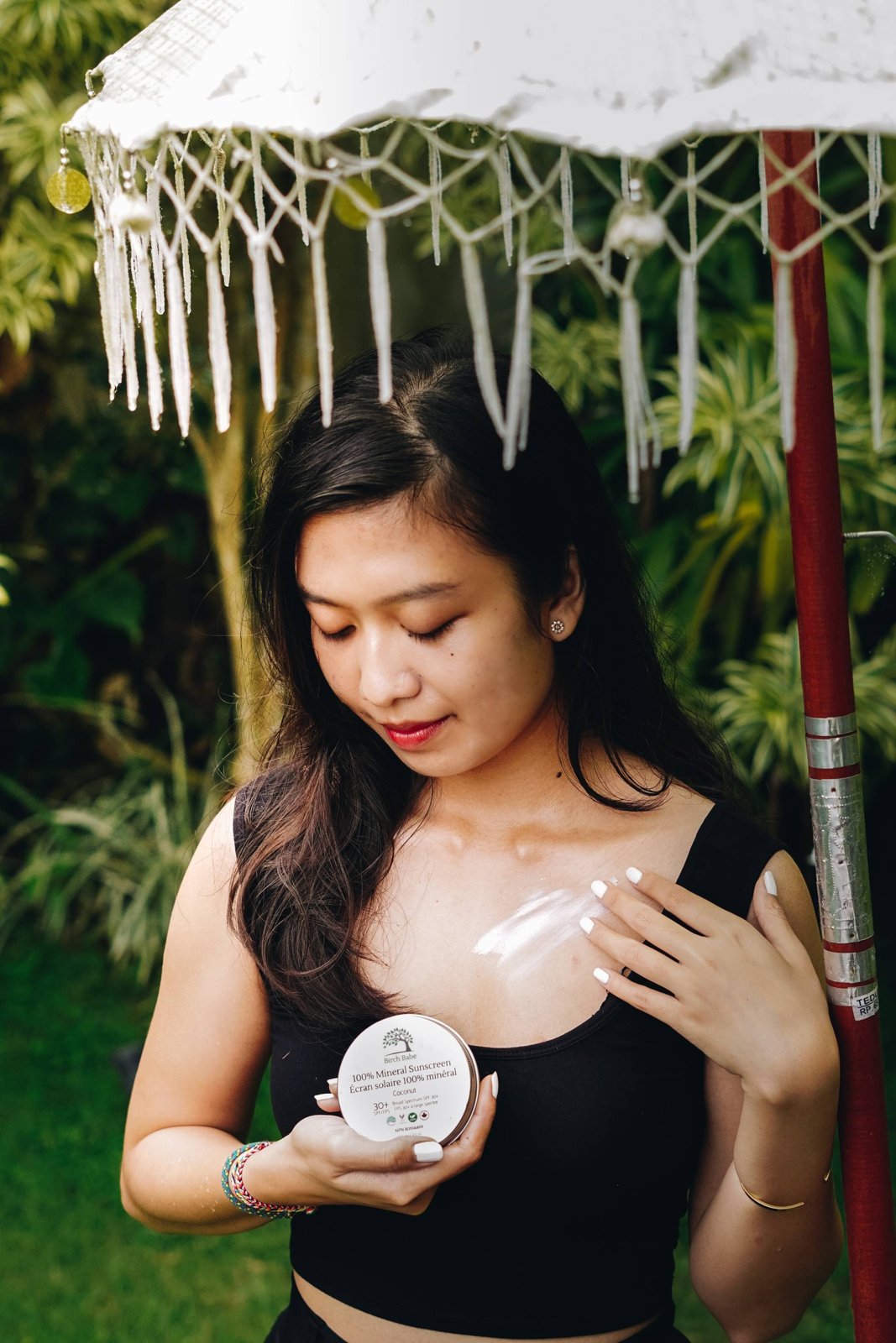 Model holding a Birch Babe skincare jar under a white fringed parasol