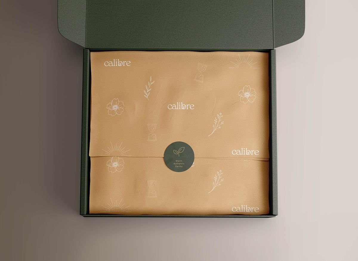 Green mailer box opened to show kraft tissue paper printed with the Calibre logo and botanical doodles
