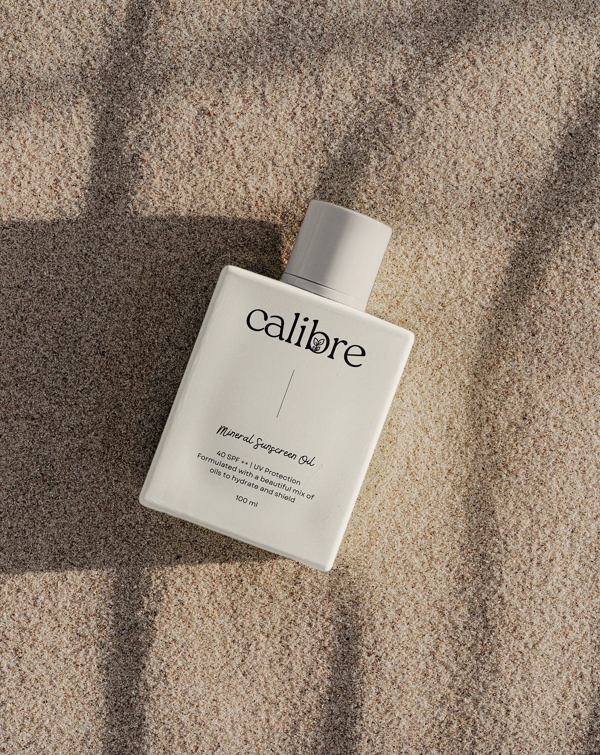 Calibre mineral sunscreen bottle lying on sand in soft shadow