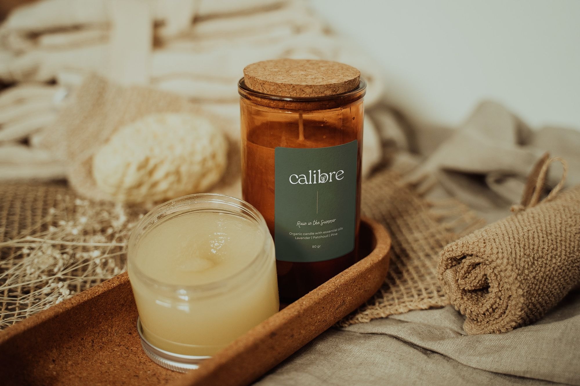 Calibre candle in an amber jar on a wooden tray with linen and a sponge