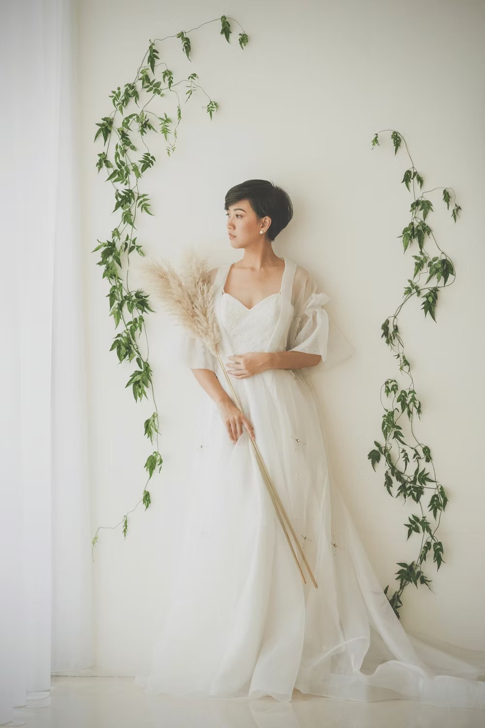 Bride in a white gown against a wall with trailing ivy