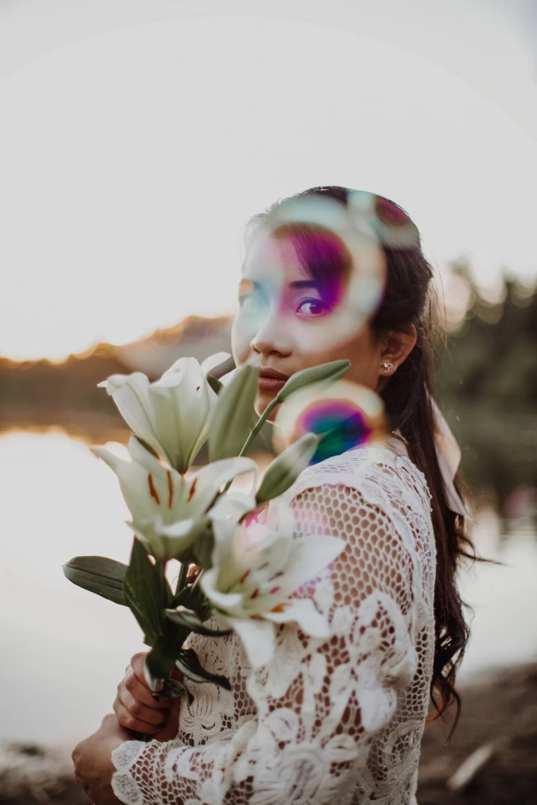 Bride in lace holding white lilies at sunset
