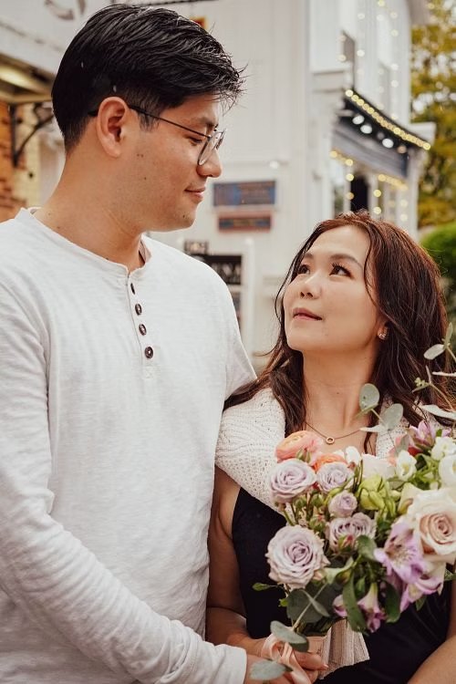 Couple gazing at each other with a pink bouquet on a city street