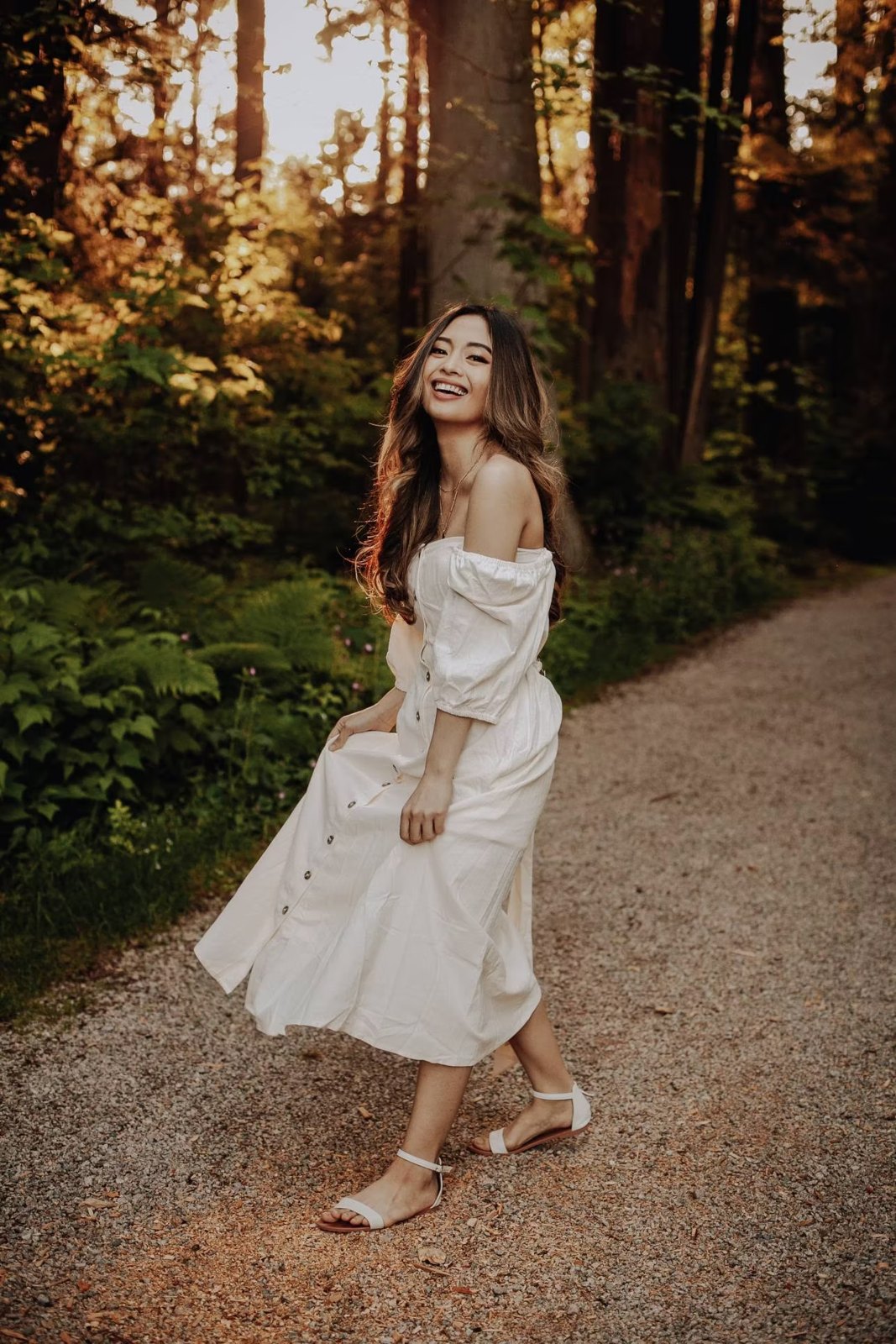 Woman twirling in a white dress on a sunlit forest path