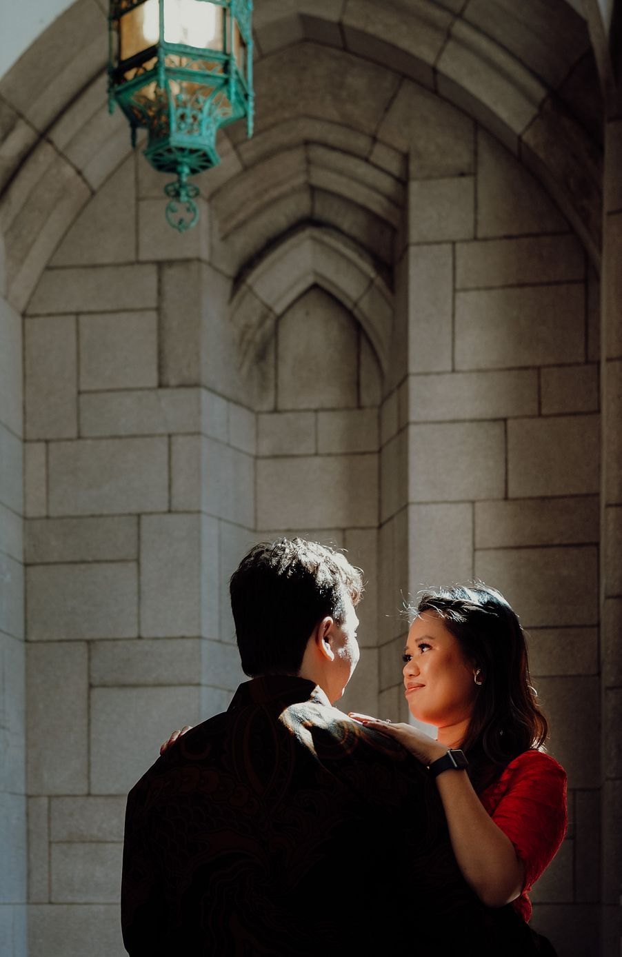 Couple embracing under a stone archway beneath a green lantern