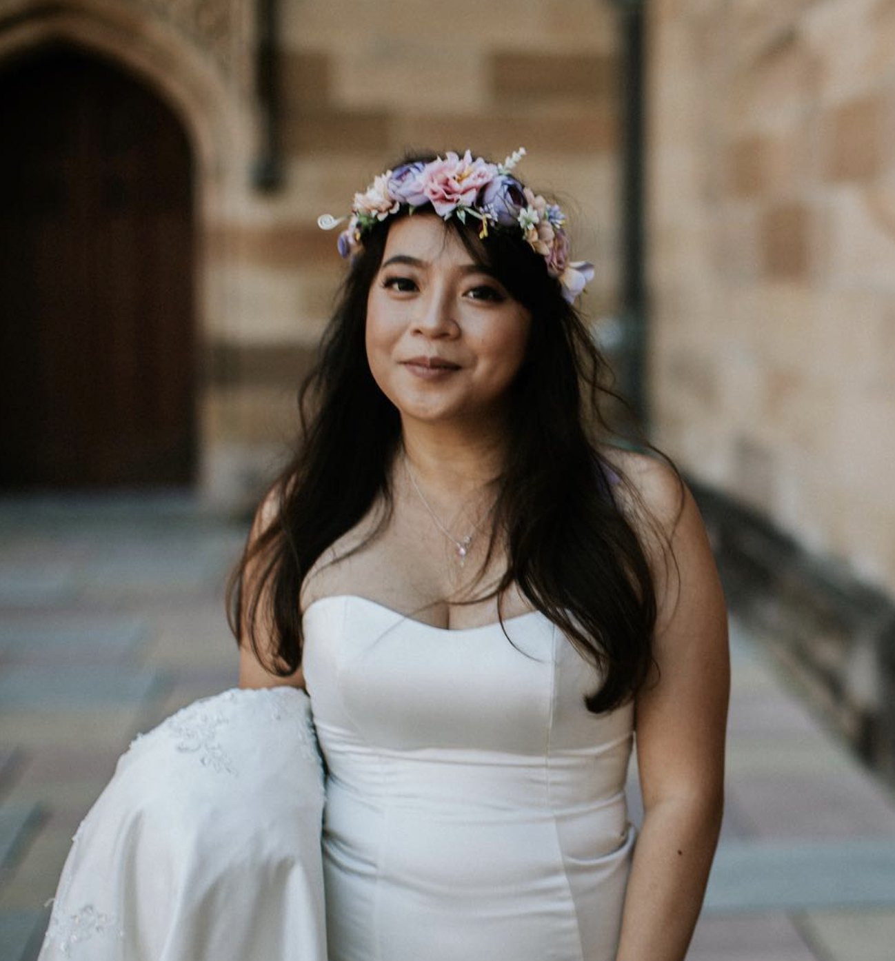Smiling bride in a strapless gown and a pastel flower crown outside a sandstone building