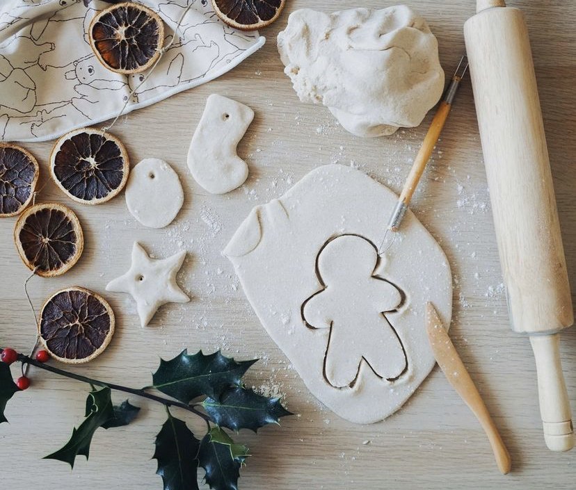 Salt dough being cut into gingerbread shapes beside dried orange slices